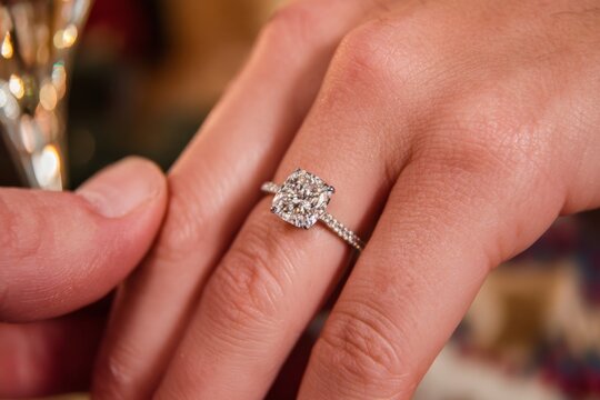 Close-up of hand wearing sparkling lab-grown diamond engagement ring with cushion cut, being shown off at engagement party. Celebration, modern proposal.