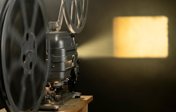 Vintage film projector plays classic movies in a dimly lit room with a bright beam of light shining on the wall