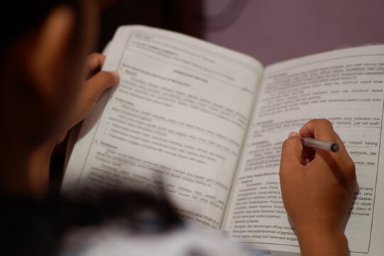 Child hands holding pen and flipping book page while reading