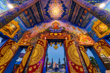 Obraz premium Interior view of the spectacular Blue Temple or Wat Rong Suea Ten with a large white Buddha statue and intricate golden Thai art murals on blue walls, Chiang Rai, Thailand.