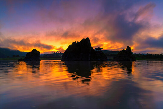 Majestic fiery sunrise silhouette of the traditional pavilion and Dodamsambong Peaks reflected on the river under a dramatic orange and purple twilight sky, Danyang, South Korea.