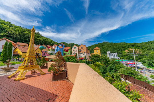 Scenic perspective of Petite France theme park featuring vibrant pastel buildings and French traditional architecture surrounded by green mountains, landmark in Gapyeong, Republic of Korea.