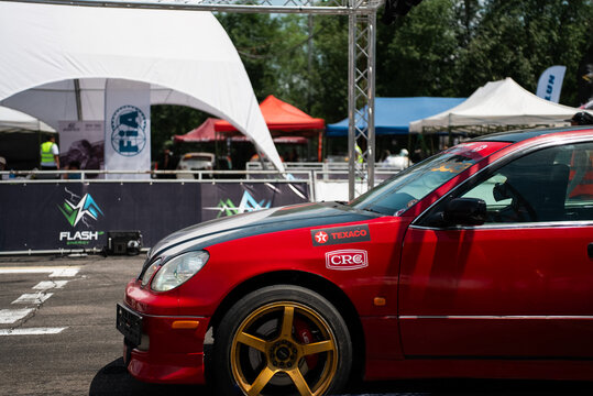 Bishkek, Kyrgyzstan - 8 June 2026: Kyrgyz Republic Drift Championship. Red modified drift car at motorsport venue, with sponsor logos, racing wheel, event tents and competition area in the background.