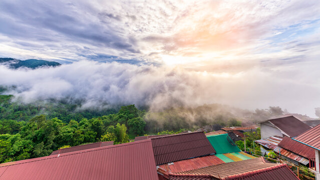 Stunning sunrise over Akha Pa Kluay mountain village in Doi Tung, Chiang Rai, Thailand, with a majestic sea of fog covering the green valley and village roofs in the foreground.
