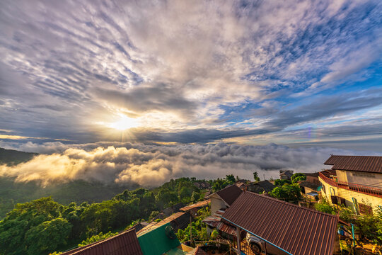 Stunning sunrise over Akha Pa Kluay mountain village in Doi Tung, Chiang Rai, Thailand, with a majestic sea of fog covering the green valley and village roofs in the foreground.