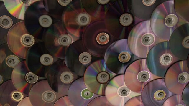 Collection of old CDs stacked together with reflections and colors in a bright room