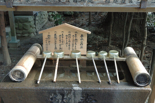 Traditional water purification pavilion (Chozuya) at a Japanese Shinto shrine with metal ladles and a wooden sign explaining the etiquette, Sendai, Japan.