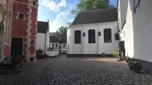 Historic Kortrijk beguinage alley motion, camera advancing through UNESCO‑listed pathways in soft daylight.