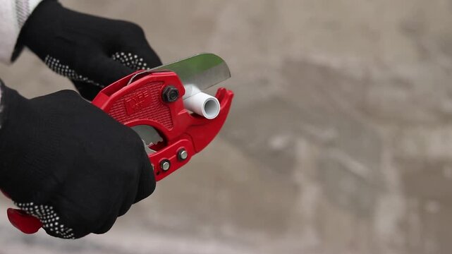 A craftsman in protective gloves cuts a polypropylene pipe using a manual pipe cutter. The process of installing plastic pipes for water supply. Manual ratchet pipe cutter for PVC and PPR pipes
