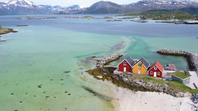 Aerial of small traditional rorbu fishing huts with snow covered mountain background on summer Sommaroy island Norway