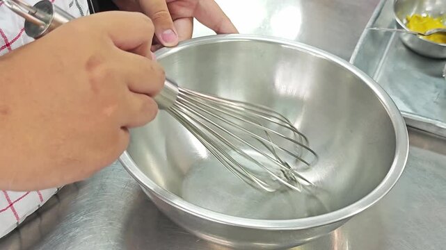 Hand holding a stainless steel whisk in a mixing bowl.