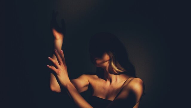 Woman in the sensually touching the skin of her arm as the shadows obscure her face