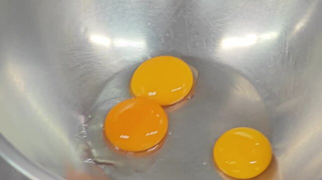 Three fresh raw egg yolks in a stainless steel mixing bowl.