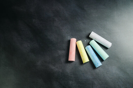Colorful chalk sticks on blackboard surface, education mockup background