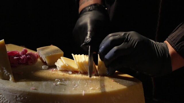 Chef hands with black gloves cutting fresh parmesan cheese on a large cheese wheel at event catering