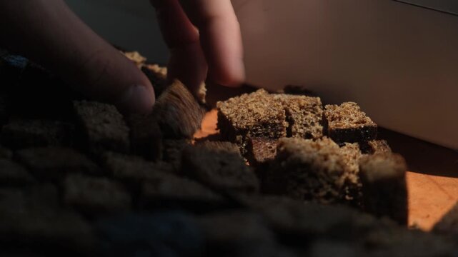 Fingers turning cubes of black croutons for even drying in sunlight. Drying dietary yeast free bread. Rye croutons. Healthy nutrition and lifestyle. Low calorie bread with fiber and low carbohydrates