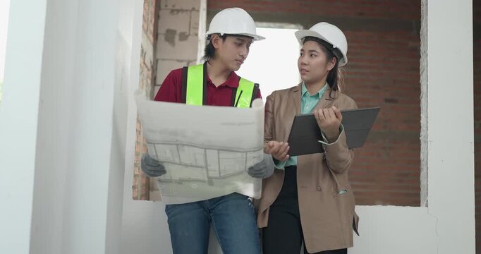Male site engineer and female architect compare printed blueprints with a digital plan at a residential construction site, checking design details against real site work.

