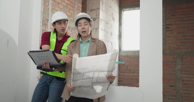 Male site engineer and female architect compare printed blueprints with a digital plan at a residential construction site, checking design details against real site work.
