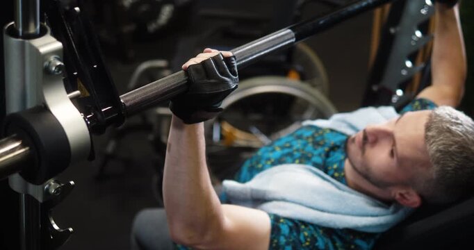 Man with disability trains shoulders and arms on a machine in the gym by grabbing a bar.