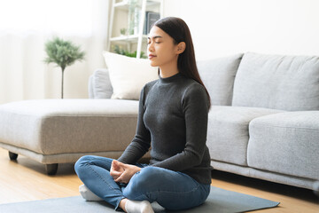 Obraz premium Beautiful asian young woman, girl hands in calm pose sitting practice meditating in lotus position on sofa at home, meditation, exercise for wellbeing, healthy care. Relaxation, happy leisure people.