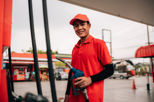 Smiling Gas Station Attendant in Red Uniform Holding Fuel Nozzle at Petrol Station