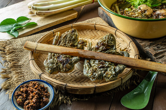 Northern Thai spicy frog soup with local herbs and vegetables, served in a yellow zinc bowl on a rustic wooden background, top view food photography. 