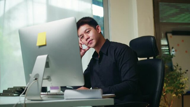 Young Asian Businessman Thinking at Office Desk with Computer Monitor and Sticky Note