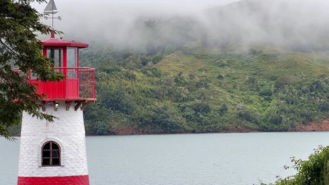static shot of a red and white lighthouse by a misty lake in calima