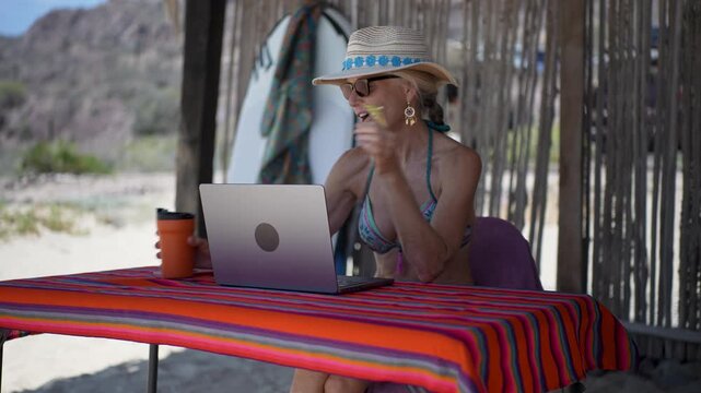 Mature woman displays emotions while using a computer on a tropical beach during her vacation time.