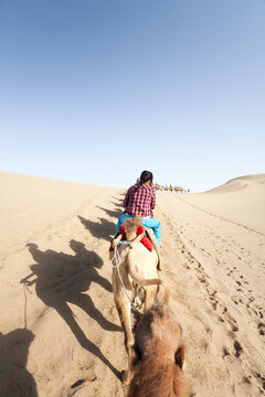 Young woman on camel caravan in the sand dunes, Dunhuang, Gansu, China