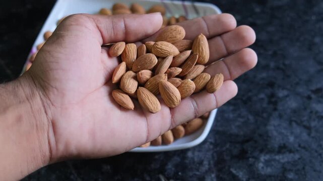 Hand holding a handful of fresh raw almonds with a bowl in the background