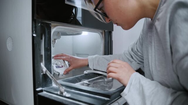 Dental technician placing a zirconia block into a cad cam milling machine for making crowns