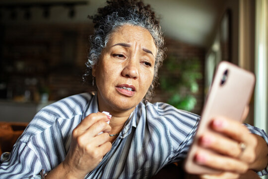 Upset mature woman with tissue looking at smartphone at home