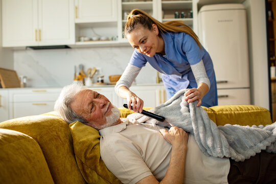 Caregiver tucking in senior man with blanket at home