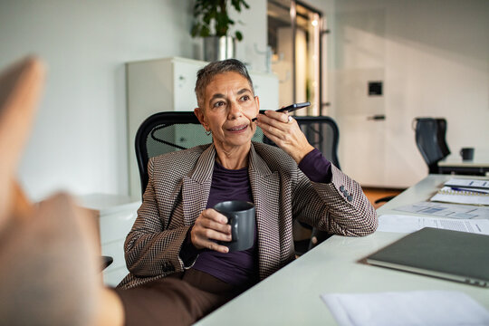 Senior businesswoman recording voice memo on smartphone at office desk