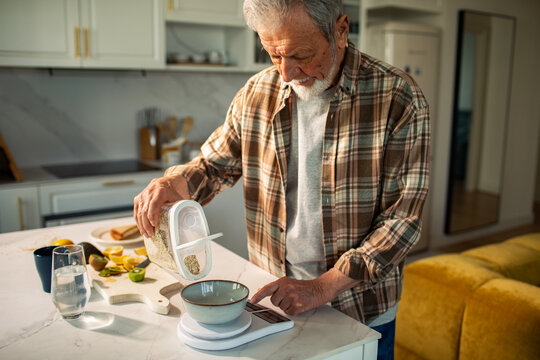 Senior man measuring oats for breakfast in home kitchen