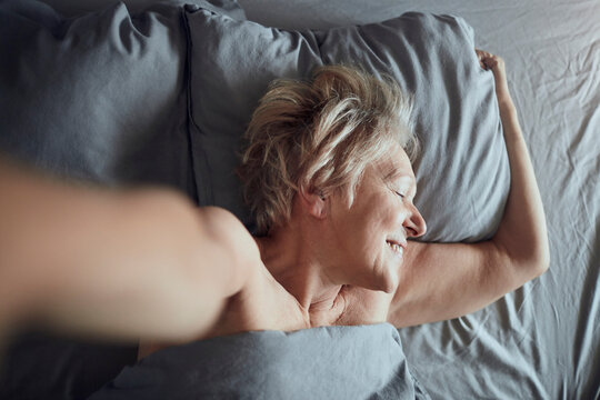 Smiling senior woman waking up and stretching in bed at home