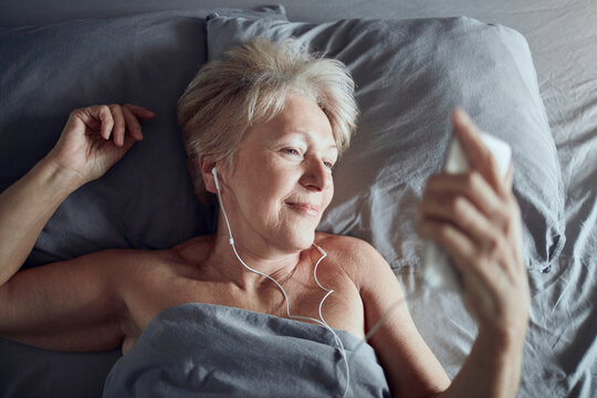 Senior woman listening to music on smartphone in bed