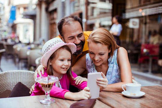 Parents and daughter looking at smartphone at an outdoor cafe
