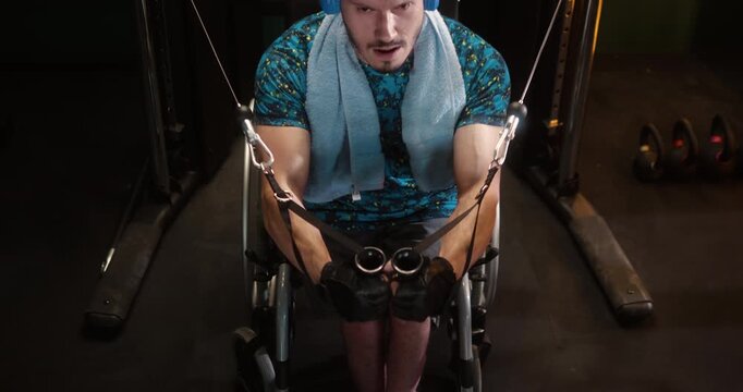 Man in wheelchair performs upper body exercise on a cable machine in gym. Focused and determined during workout, demonstrating an active lifestyle despite physical disability.