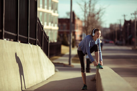 Young woman tying running shoe on urban sidewalk