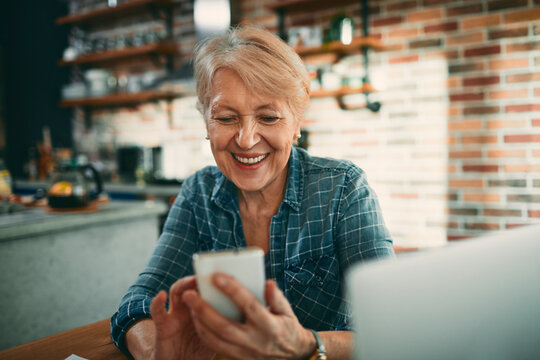 Smiling senior woman using smartphone in home kitchen