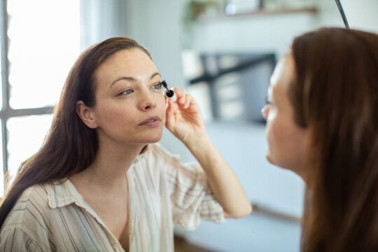 Woman applying mascara in bathroom mirror at home