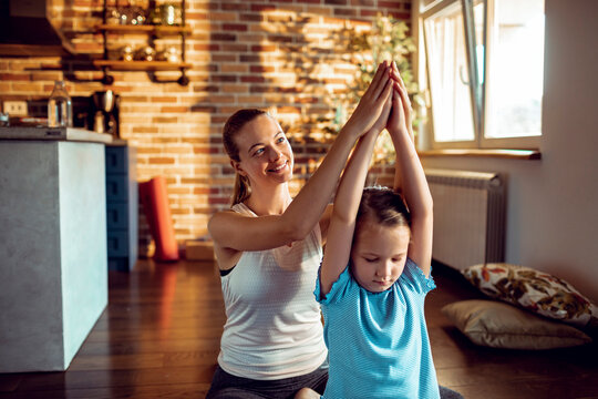 Smiling mother helping daughter with yoga pose at home