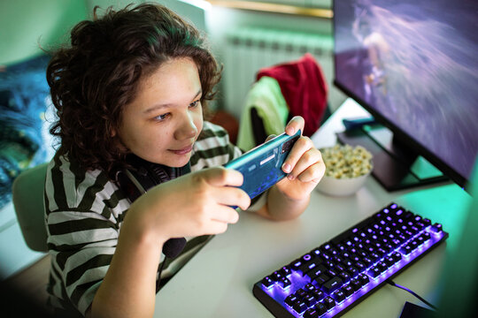 Teen gamer playing on smartphone at home computer desk