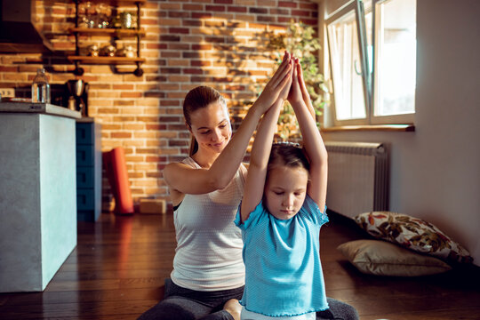 Mother guiding daughter in yoga practice at home