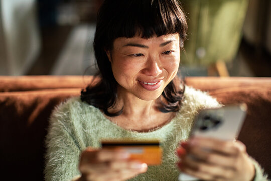 Smiling woman shopping online with credit card on smartphone at home