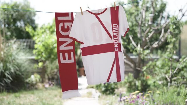 Football fan t-shirt and scarf supporting England hanging on clothesline outdoors in garden on sunny windy summer day
