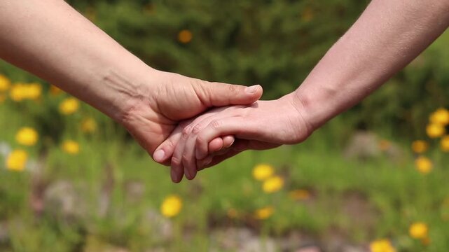 Couple holding hands on nature background. Close-up of hands of man and woman intertwined with fingers during a walk. Concept of love. Two people holding hands on a background of flowers