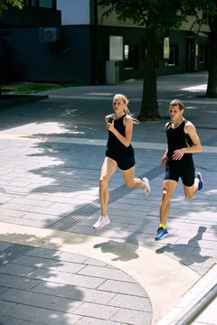 Focused running pair crossing city walkway in bright daylight. Concept of urban workout routine, fitness app visuals, endurance training, and wellness campaign content.